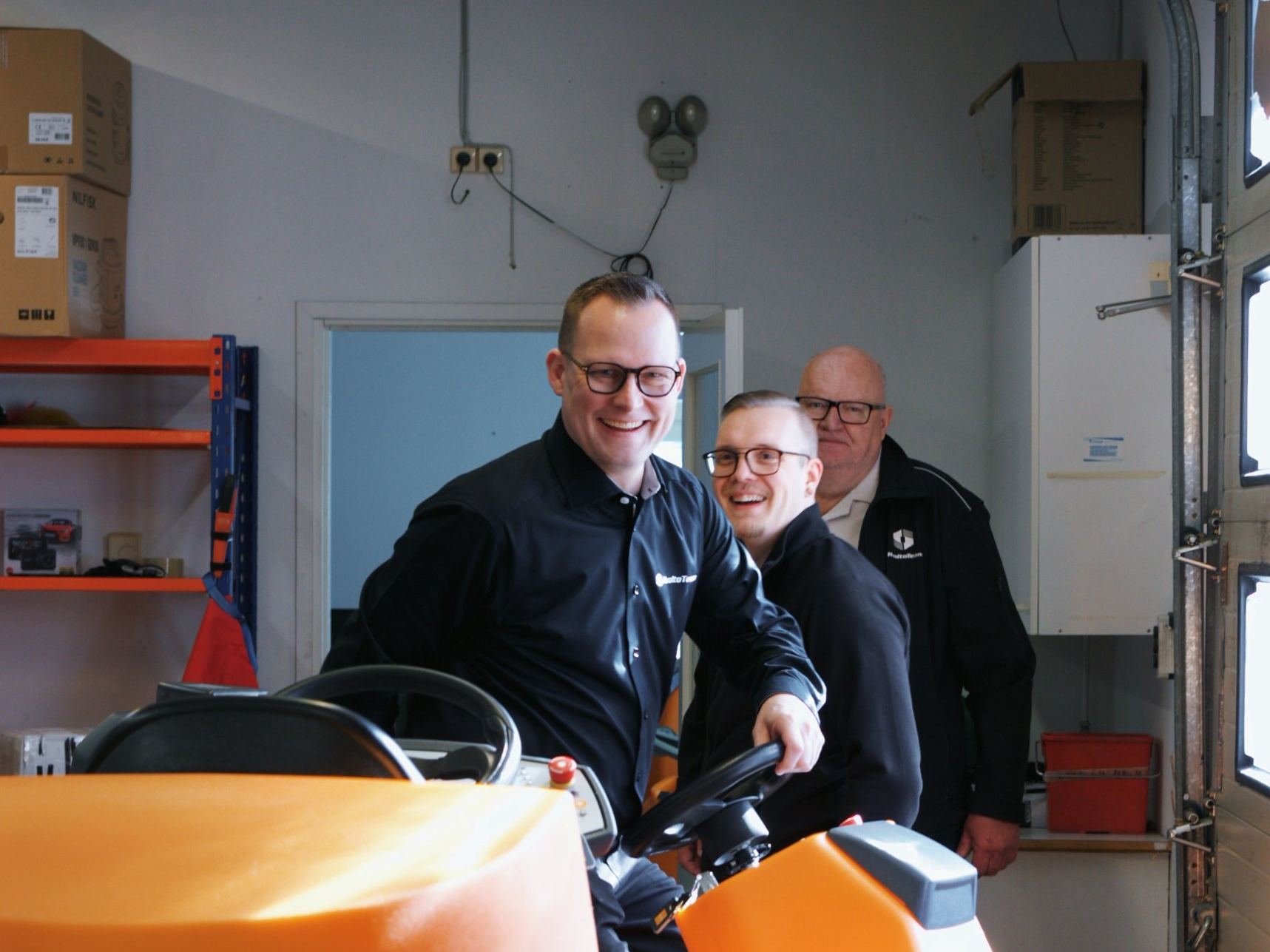 HuoltoTeamin kolme työntekijää hymyilee korjaamolla ajettavan TASKI-siivouskoneen ääressä