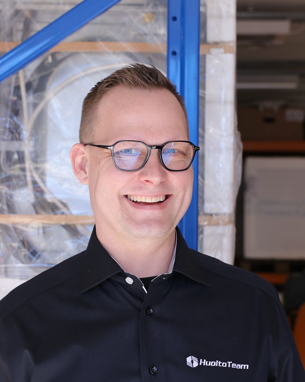Hymyilevä HuoltoTeamin työntekijä varaston hyllyjen edessä